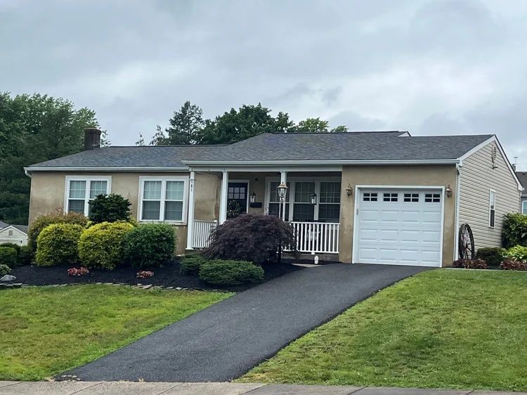 Single-story suburban house with a garage, driveway, and front lawn under cloudy skies