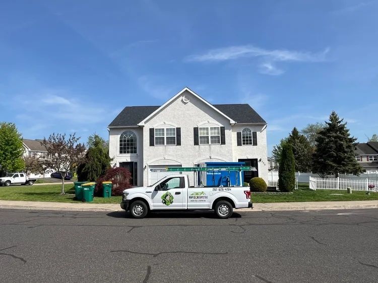 White utility van parked in front of a two-story house on a suburban street, with blue equipment on top
