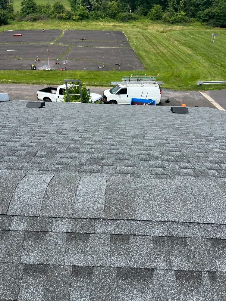 Roof shingles overlooking white utility vans and a grassy field with a dark paved area beyond.