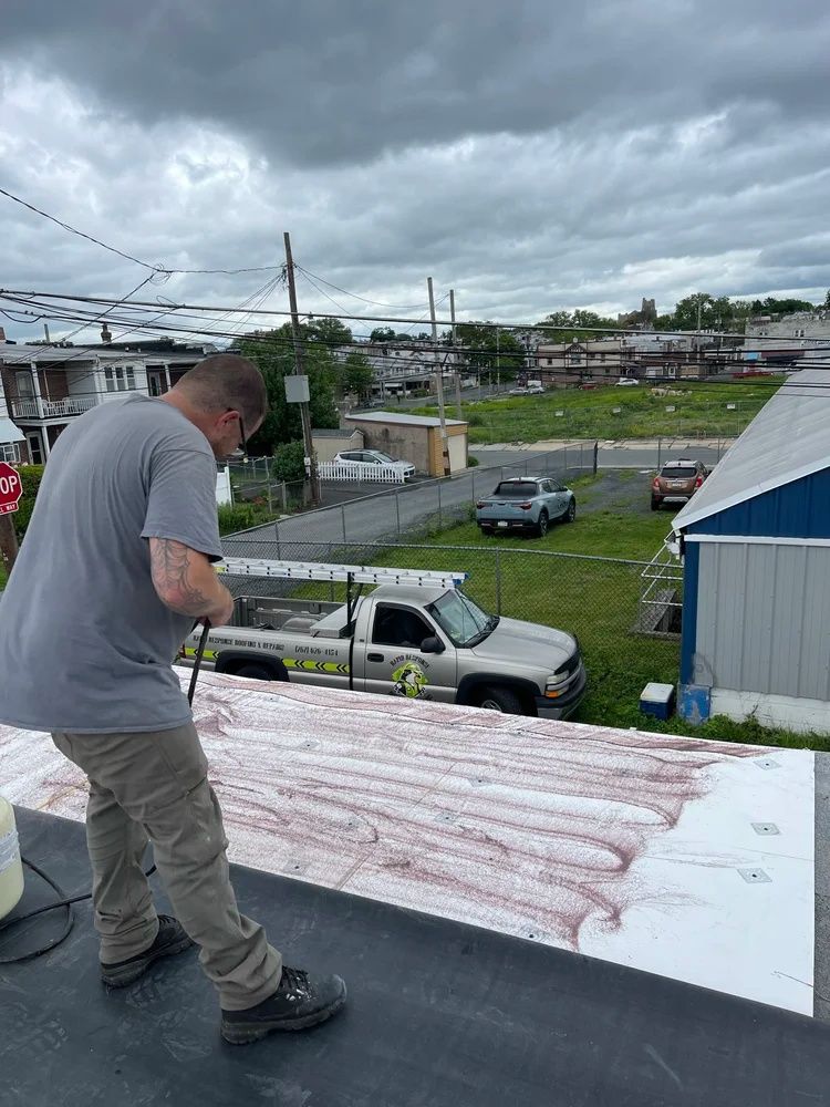 Worker spreading sealant on a flat roof under cloudy skies