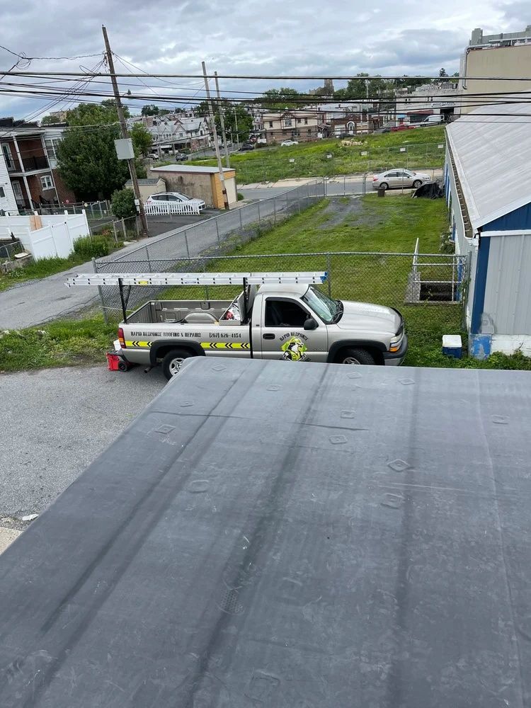 White pickup truck parked by a fence beside a wet street in a neighborhood, viewed from a rooftop