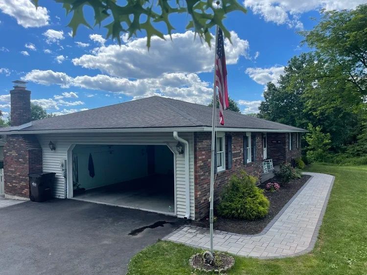 Brick house with open garage, American flag, and landscaped driveway under a blue sky