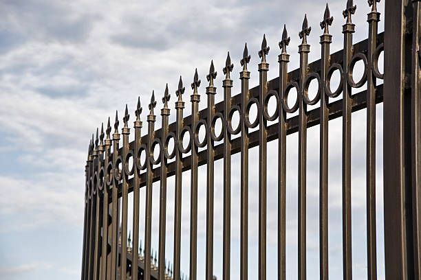 A close up of a metal fence with a cloudy sky in the background.