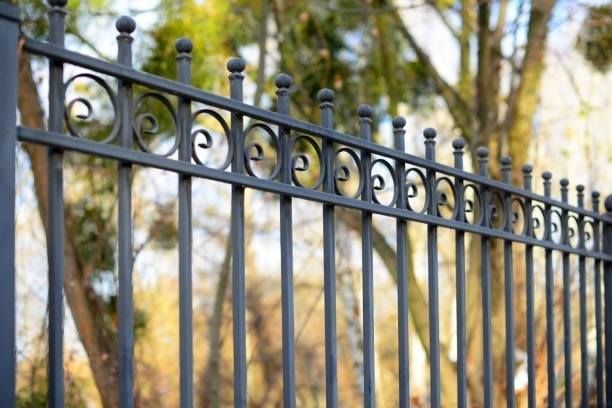 A close up of a wrought iron fence with trees in the background.