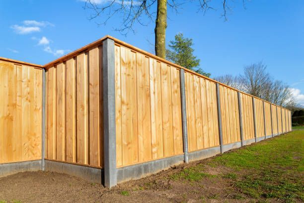 A wooden fence with concrete posts and a tree in the background.