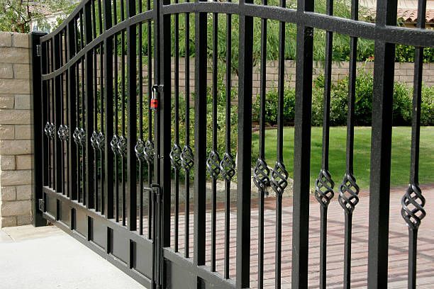 A black wrought iron gate is open to a driveway.