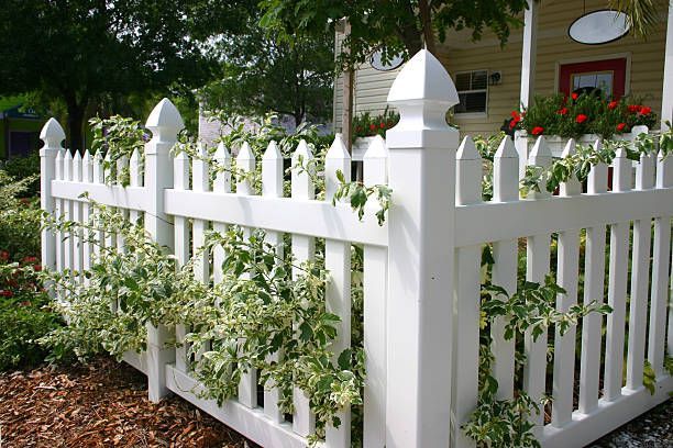 A white picket fence surrounds a house with flowers on the porch.