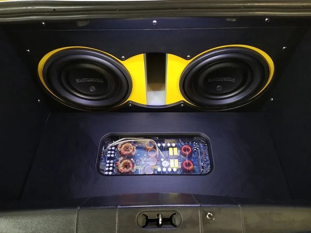 Car trunk with two yellow-accented subwoofers and an amplifier; black interior.