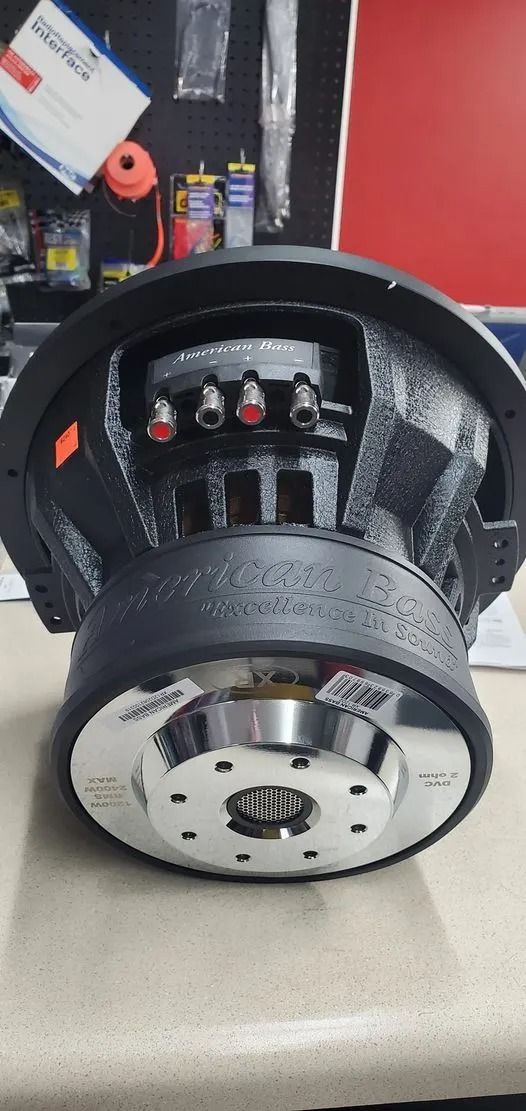 Black subwoofer with silver accents, on a light-colored surface. Red and silver terminals visible.