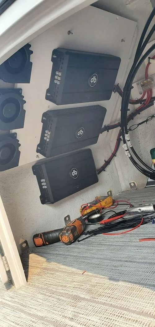 Three black audio amplifiers mounted on a white surface, with wiring and tools visible.