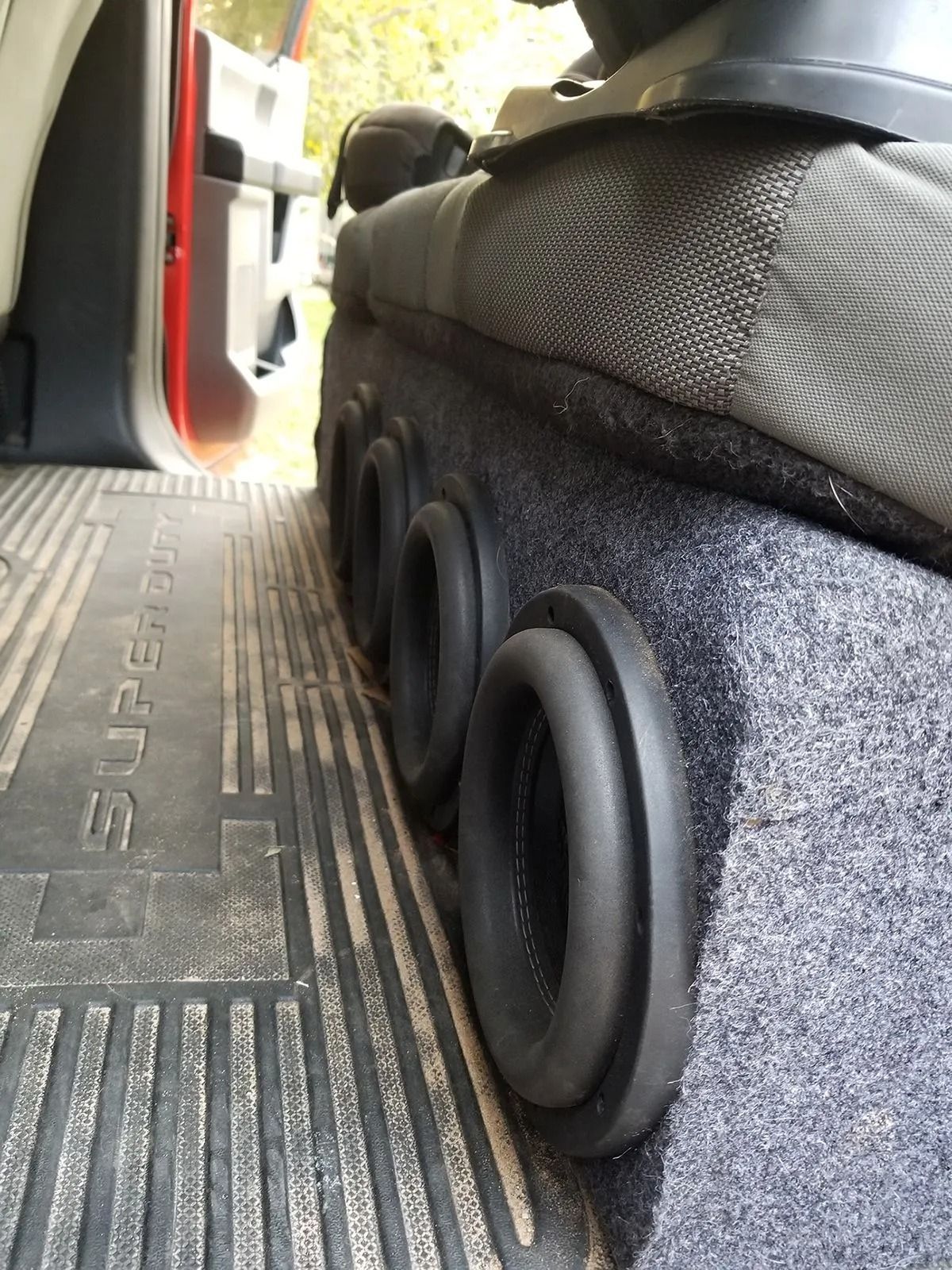 A subwoofer box with four ports in a truck. The box is under the driver's seat on a Super Duty floor mat.