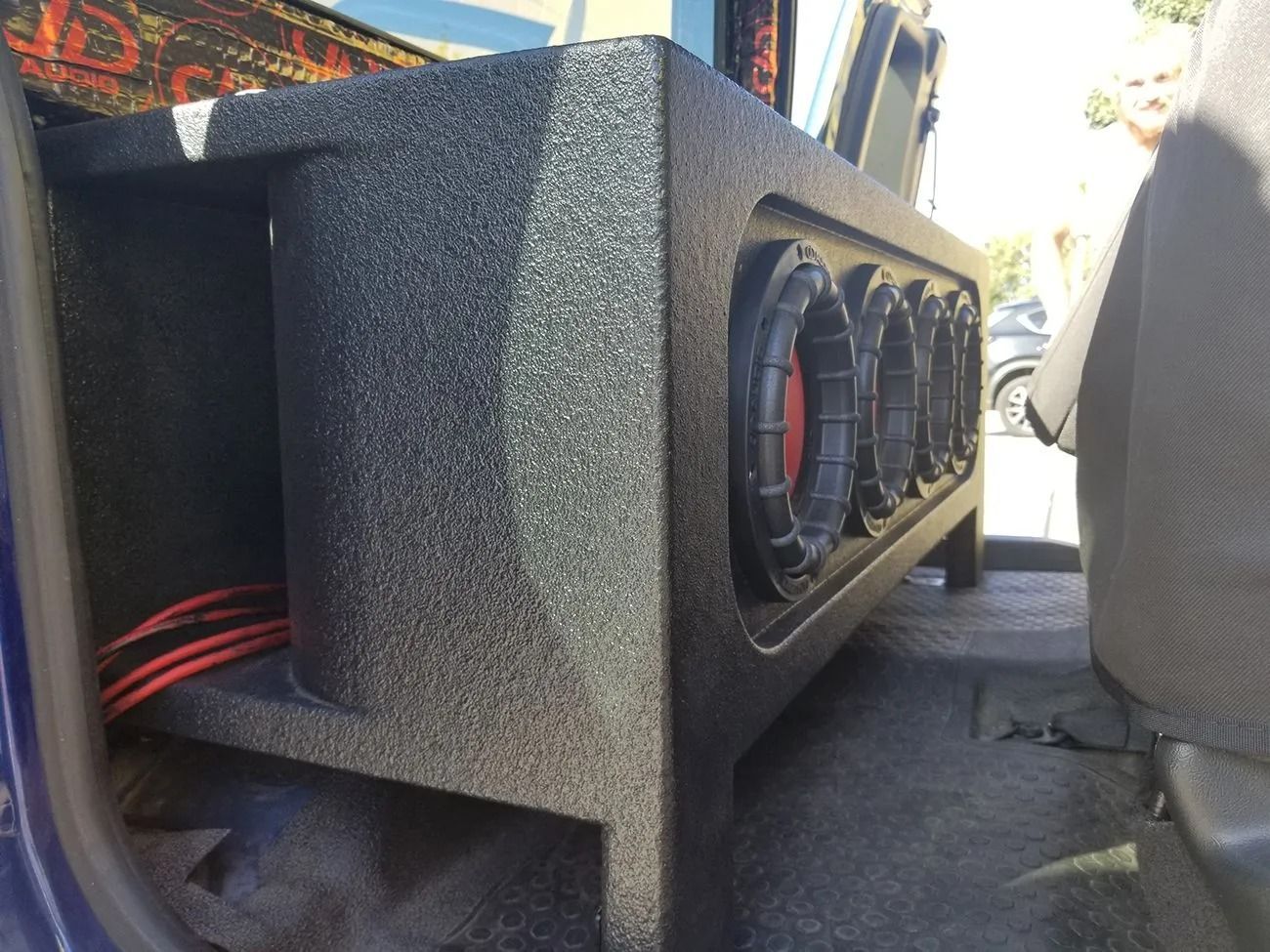 Black subwoofer box with six speakers in a vehicle, red wiring visible.