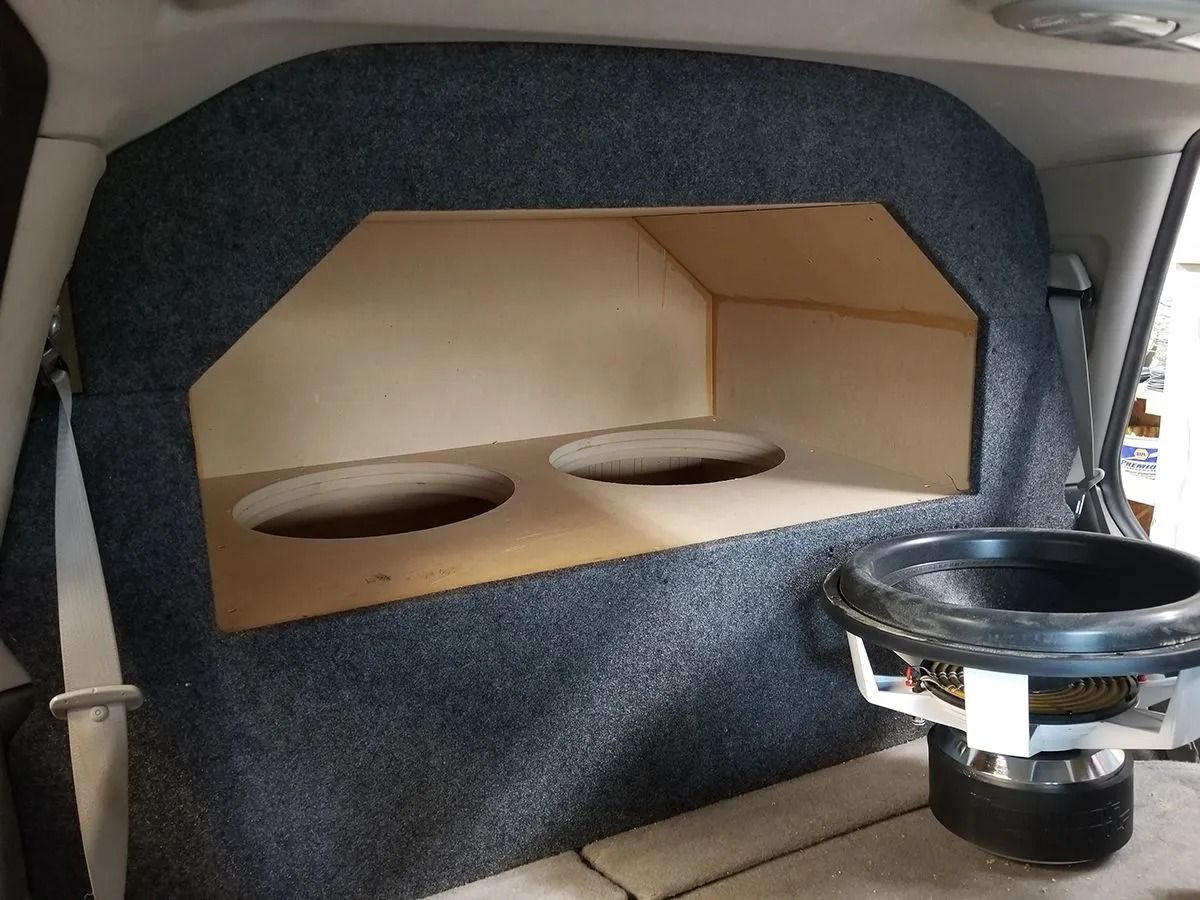 Custom car audio subwoofer box with two speaker holes, covered in grey carpet.