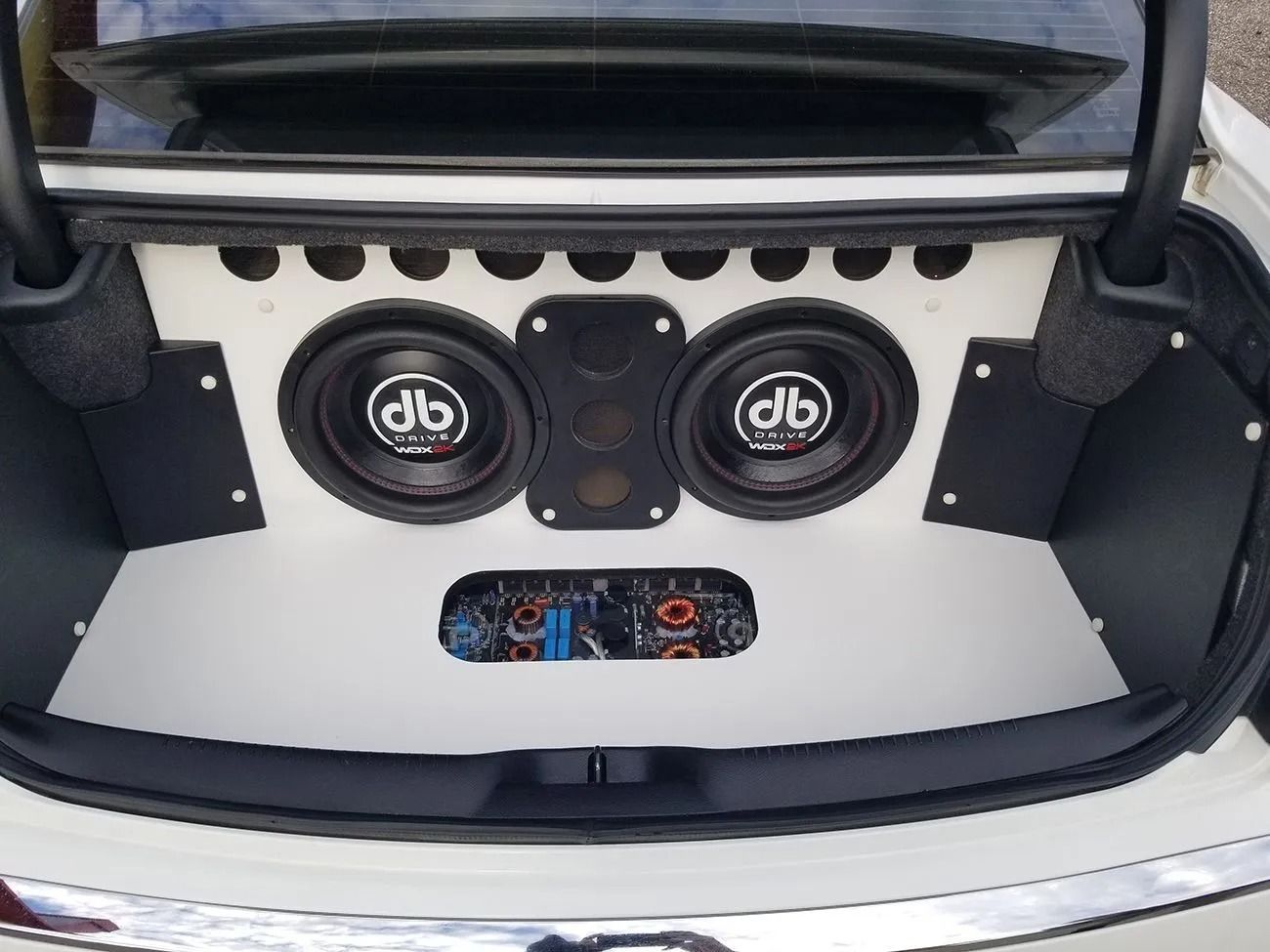 White car trunk with custom audio installation. Two subwoofers, speakers, and amplifiers.