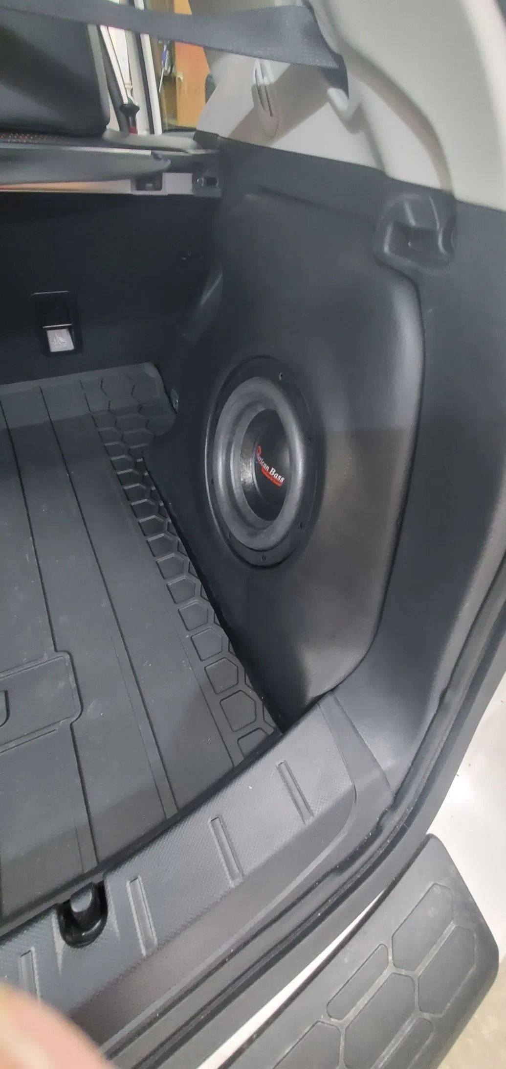 Car trunk with a subwoofer installed on the side. Black interior, with a rubber mat.