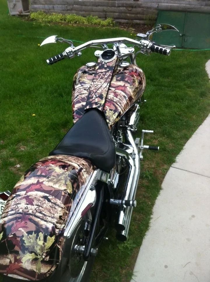 Camouflage-painted motorcycle parked on grass next to a sidewalk. Chrome details.