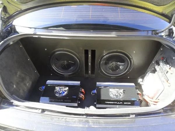 Car trunk with two subwoofers and two amplifiers, black interior, audio system.