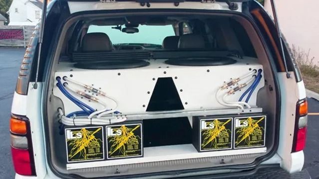 White SUV trunk with custom audio system; two large subwoofers, four amplifiers, and wiring.