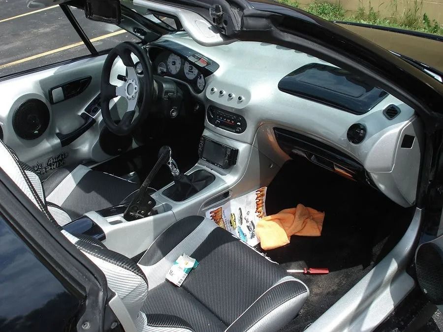 Black and silver car interior with custom dashboard, seats, and steering wheel; a magazine and orange cloth are visible.