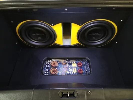 Car trunk with two yellow-accented subwoofers and an illuminated amplifier panel.
