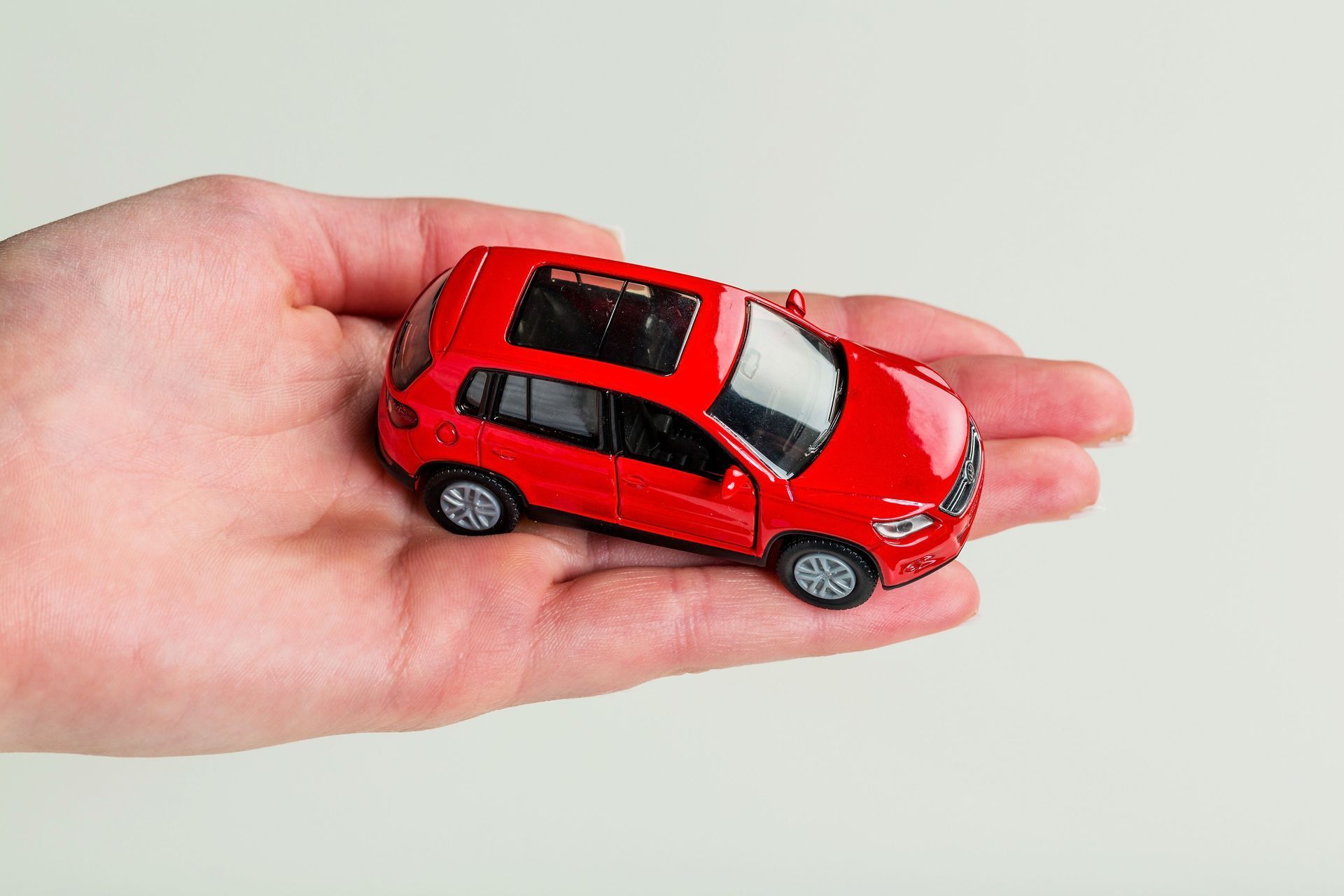 Hand holding a small red toy car with a sunroof.