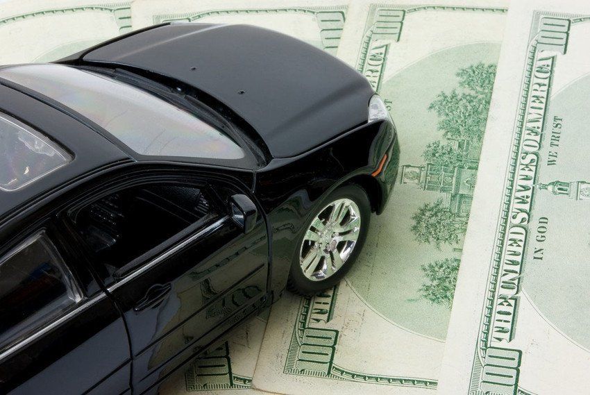 Black toy car on top of scattered $100 bills.