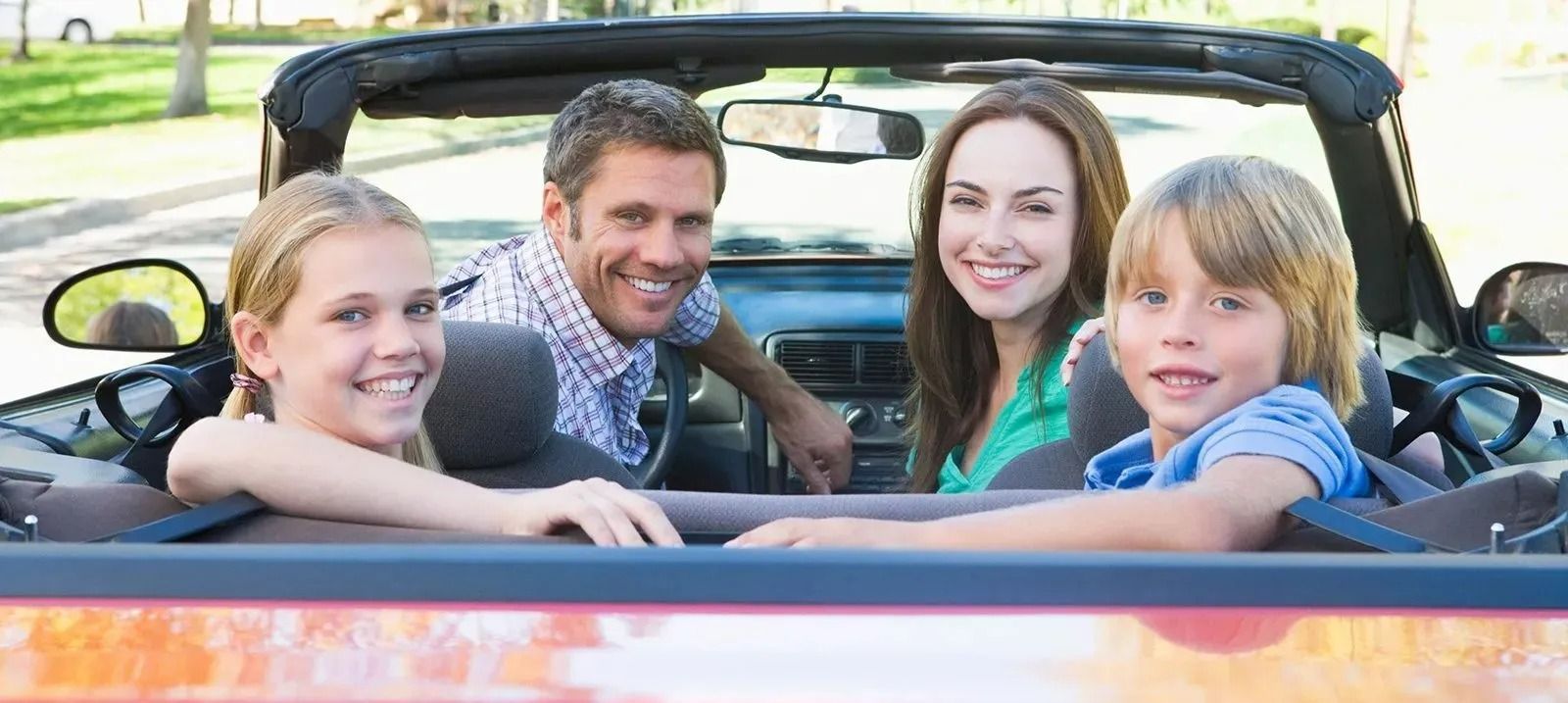 Family of four smiling in a convertible.