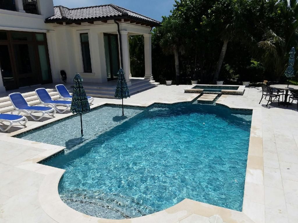 A large swimming pool surrounded by chairs and umbrellas in front of a house