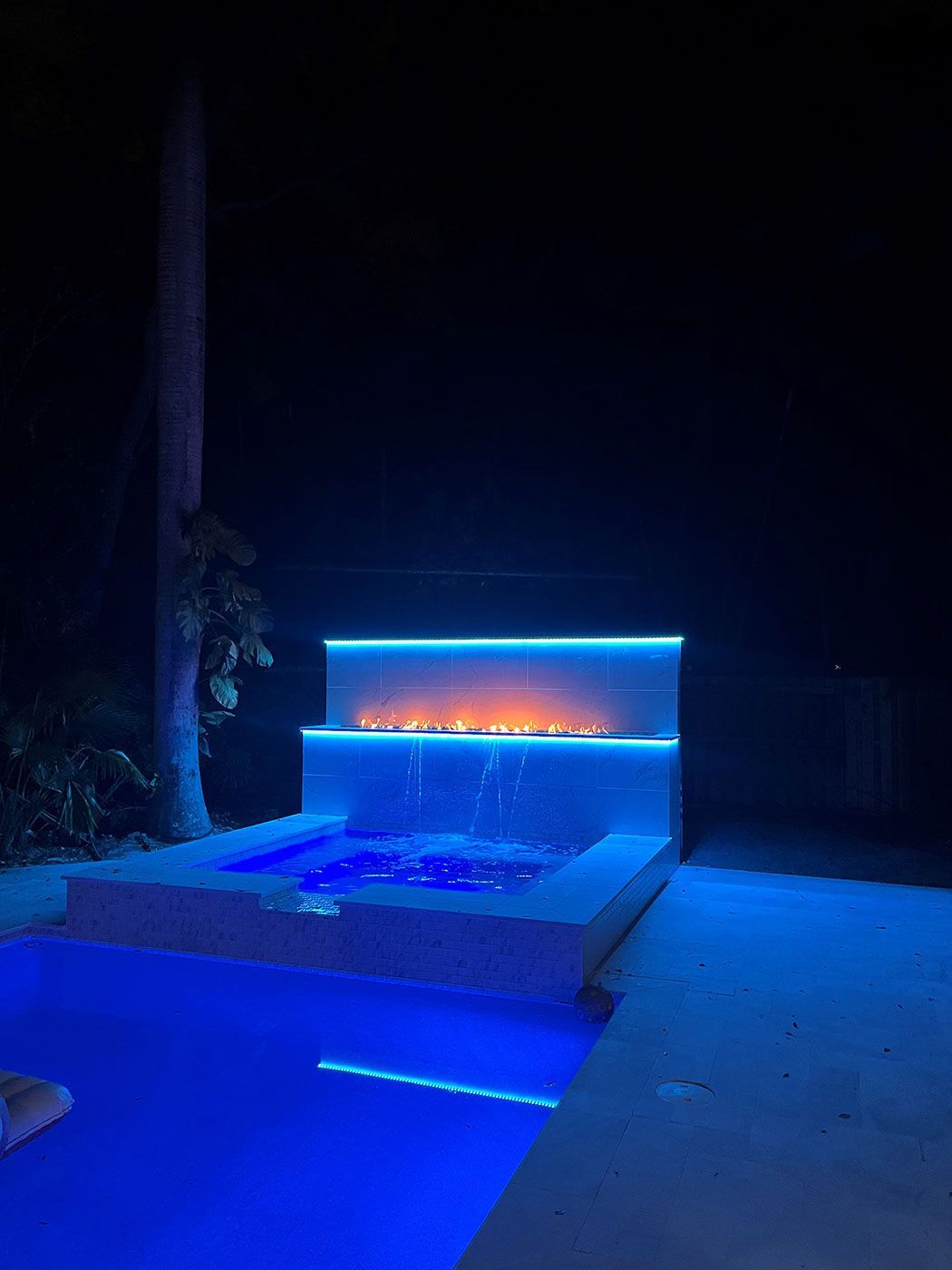 A swimming pool with a fireplace in the middle of it at night.