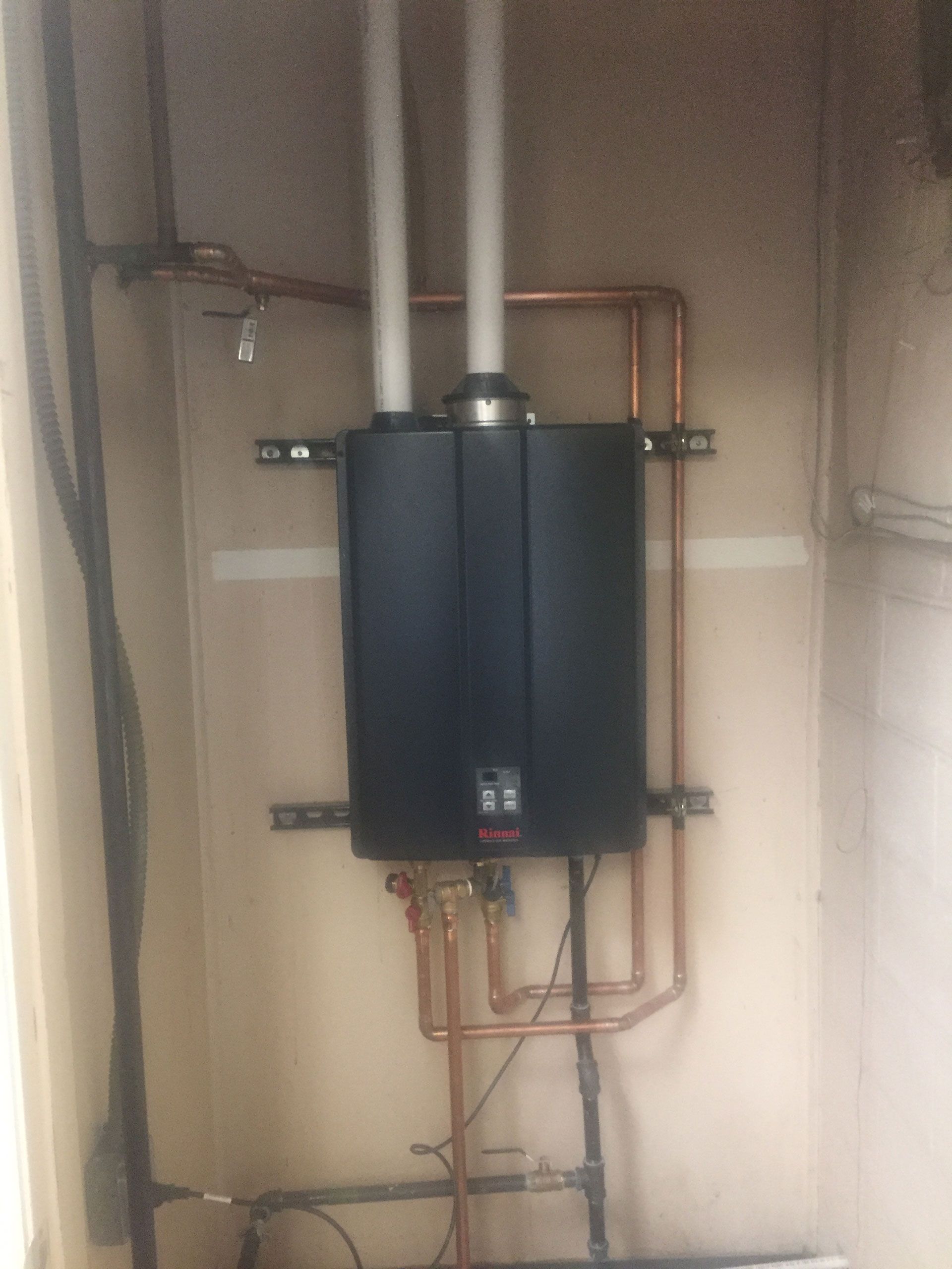 A black water heater is hanging on a wall next to copper pipes