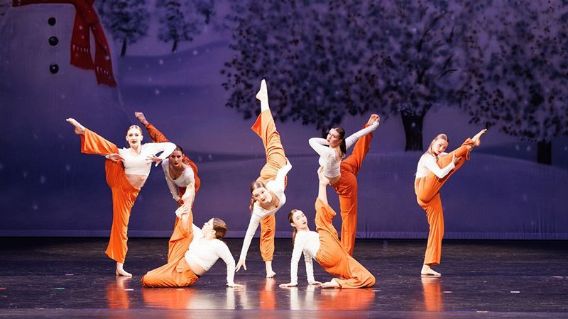 A group of dancers are performing on a stage with a snowman in the background.
