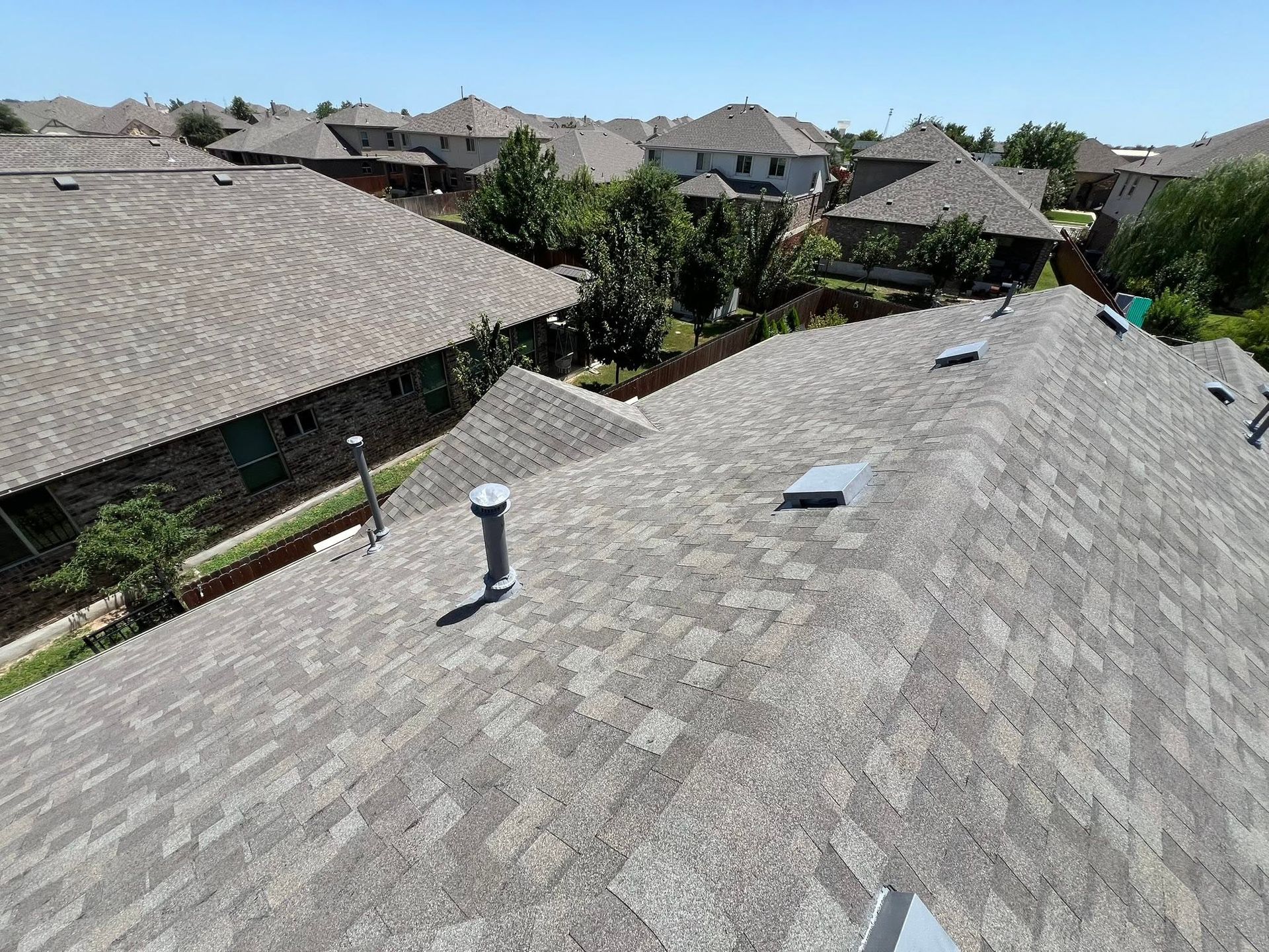 Roofline view of a suburban neighborhood with gray shingle rooftops and a few skylights under a clear sky