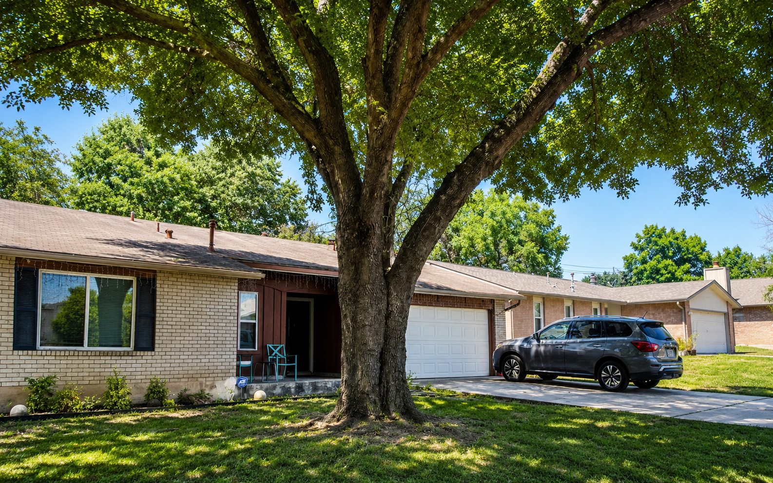 Single-story suburban house with large tree in front and a car parked in the driveway
