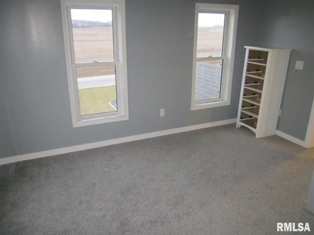 An empty room with a dresser and two windows with rmlsa written on the bottom