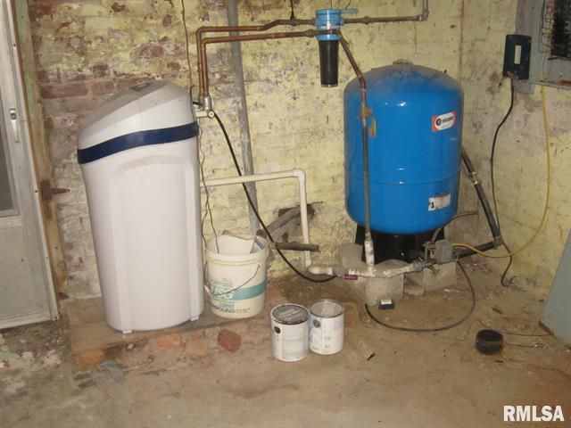 A blue water tank is sitting next to a water softener in a basement.