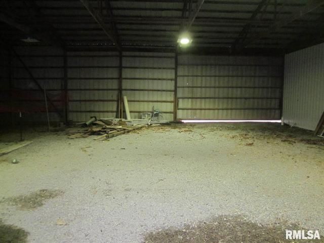 A large empty warehouse with a door open and a lot of dirt on the floor.