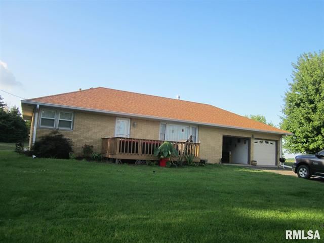 Yellow brick house with a brown roof, deck, and attached garage, on a grassy lawn.