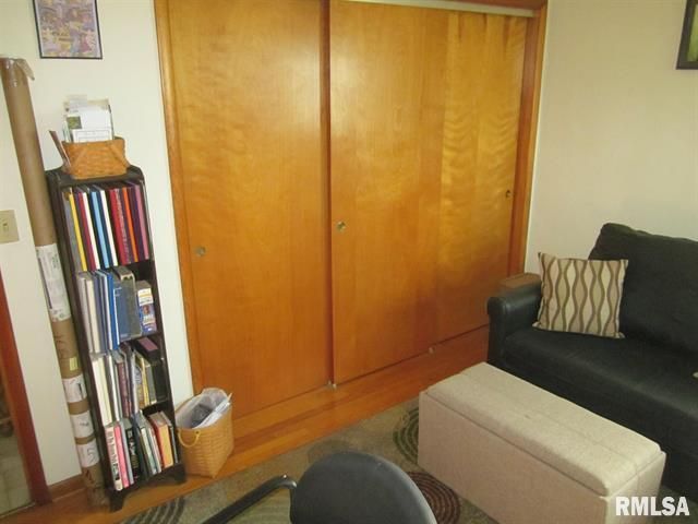 Wooden closet, bookcase with books, black couch with pillow, beige ottoman in room.
