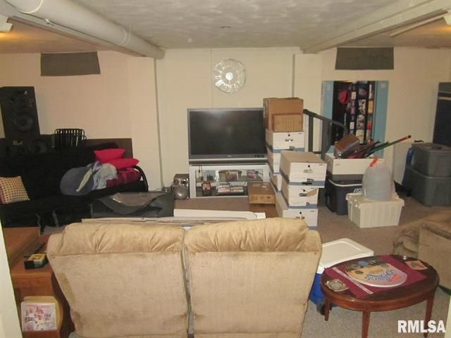 Cluttered basement with furniture, boxes, and a TV against the wall. Beige walls, white ceiling beams.