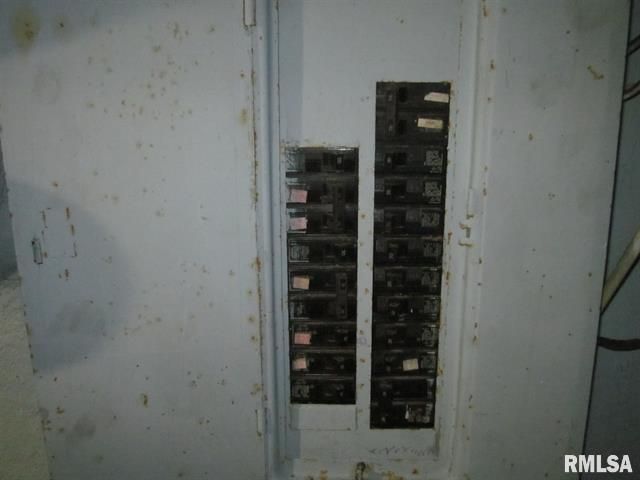 A metal electrical panel with several circuit breakers, mounted on a gray wall