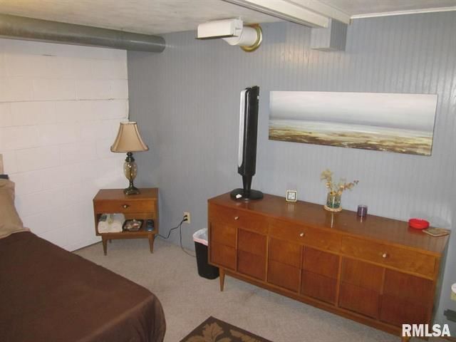 Bedroom with wood dresser, nightstand, TV, artwork, bed, and gray paneled walls.