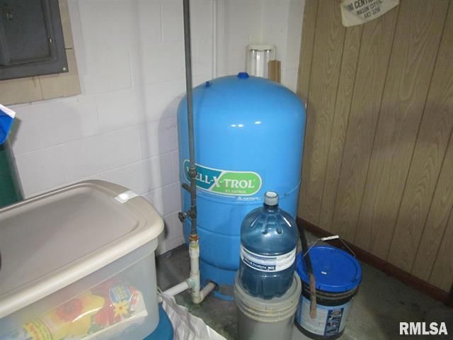 Blue well pressure tank in a basement. A water jug and bucket are beside it.