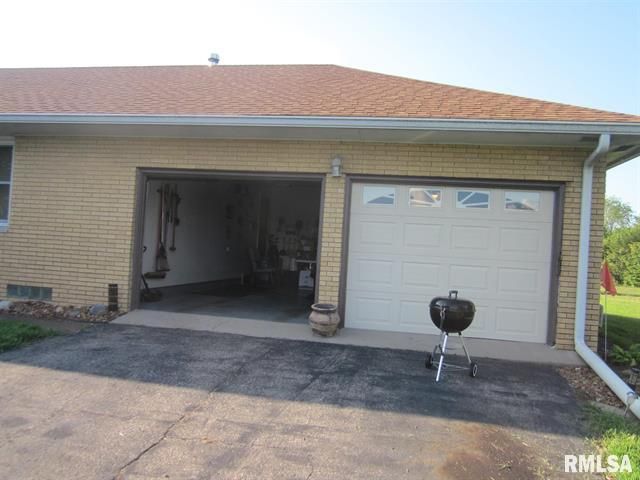 Two-car garage with one open door; tan brick exterior and a black grill in the driveway.