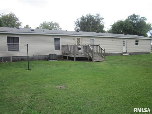 Back view of a beige mobile home with a wooden deck and green lawn