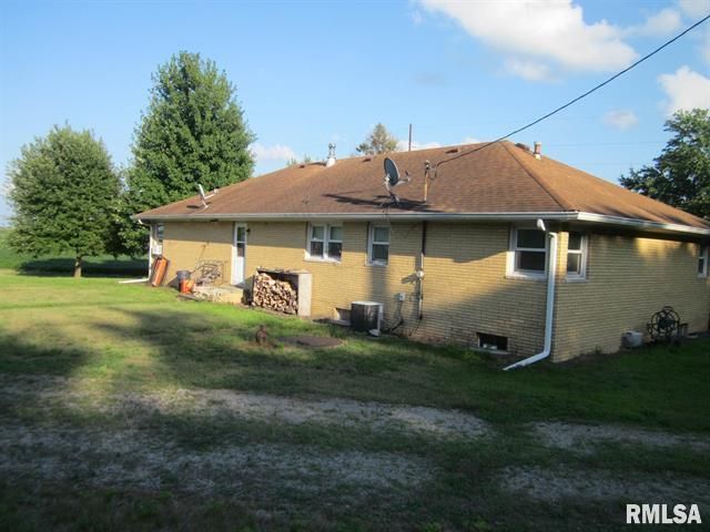Yellow house with a brown roof in a grassy area on a sunny day.