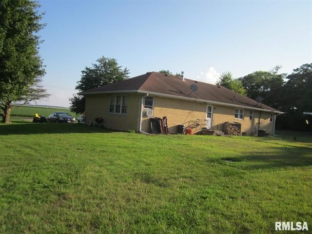Tan ranch-style house on a grassy lot, with a few cars visible in the distance.