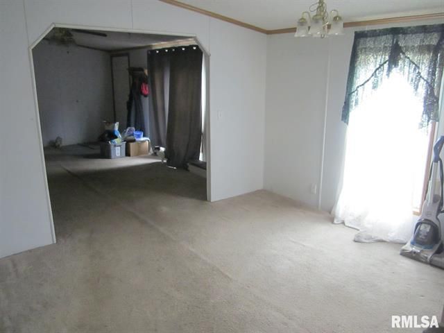 Empty interior of a home with carpet floors, white walls, and an arched doorway leading to another room