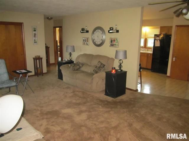 Cozy living room with brown carpet, beige walls, sofa, lamps, and a view of the kitchen.