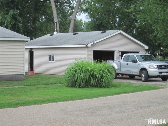 Tan garage with a pickup truck parked in front, green grass, and small building on the left