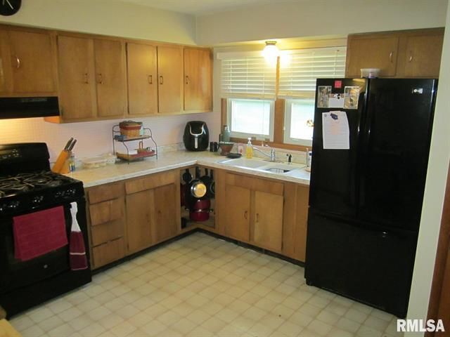 Kitchen with wood cabinets, white countertops, black appliances, and beige tile floor.